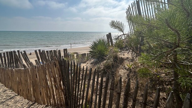 Una playa con valla de madera, orilla arenosa y vista al océano.