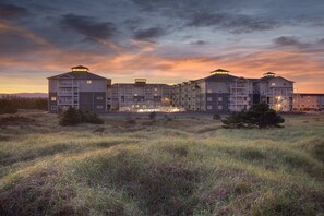 A multi-story residential building with a flat roof and multiple balconies, surrounded by grassy fields and a sunset sky. - WorldMark Long Beach - 1 Bedroom (Long Beach)
