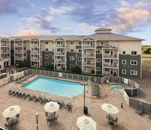 A multi-story hotel with a swimming pool, outdoor seating, and a landscaped area.