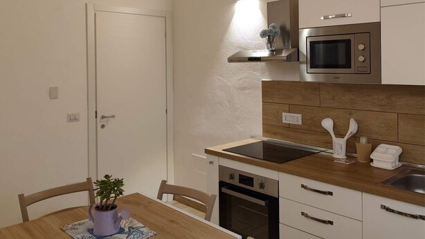 A compact kitchen with white cabinets, a microwave, a sink, and a wooden dining table with chairs. - Stay in the heart of Tropea - the sea is just a 5-minute walk away (Tropea)