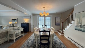 A dining area with a round table, chairs, and a chandelier. There is a staircase to the right and a sofa with a lamp in the background. - Expansive Family Home with Water Views (Marion)