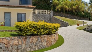Un sendero pavimentado que conduce a un edificio con un muro de piedra, un pequeño jardín y una cerca.