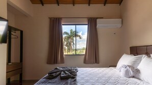 Un dormitorio con cama, ventana con cortinas, televisor en la pared y techo de madera.