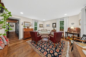 A spacious living room with a large rug, wooden furniture, and a view of the outdoors through the windows.