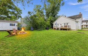 A backyard with a fire pit, a white house, and a garage.