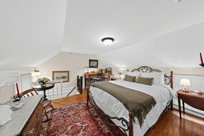 A bedroom with a bed, bedside table, lamp, and a desk with a chair.
