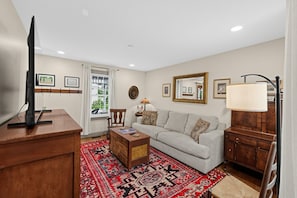 A living room with a television, a sofa, a coffee table, a patterned rug, and a window with curtains.