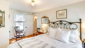 Une chambre à coucher avec un grand lit, un fauteuil à bascule, un bureau avec une lampe et un tableau encadré au mur.