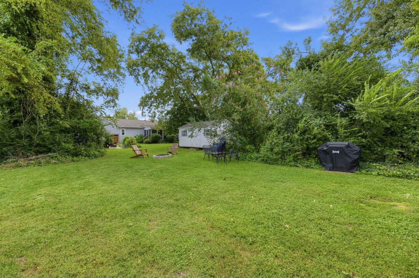 A backyard with a grill, chairs, and a small house.