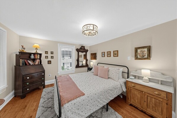 A bedroom with a bed, dresser, nightstand, lamp, and a ceiling light fixture.