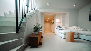 Ein modernes Wohnzimmer mit Treppe, einem Holztisch, einem weißen Sofa und einer Spielkonsole.