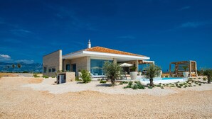 Ein modernes Haus mit Ziegeldach, großen Fenstern und einem Poolbereich mit Liegestühlen.