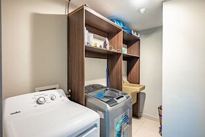 A laundry area with a front-loading washer, a stacked washer and dryer unit, and a shelf above the dryer holding cleaning supplies. - 7 Bedroom Penthouse Mountain & Ocean Views JB21001 (Jaco)