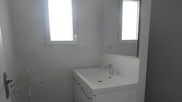 Une salle de bain avec des carreaux blancs, un lavabo, un miroir et une fenêtre.