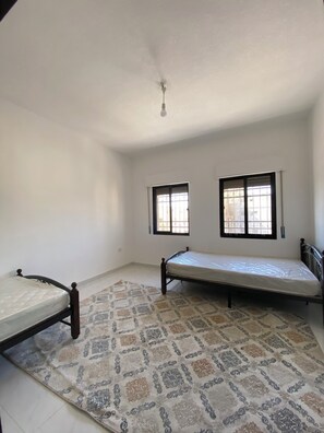 A room with two beds, a patterned rug, and two windows with blinds.