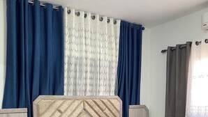 Un dormitorio con cama, cortinas, mesita de noche y mesilla.