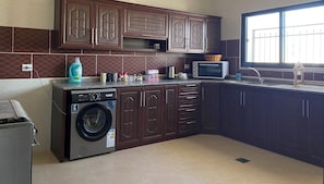 A kitchen with dark wooden cabinets, a washing machine, a microwave, and a sink.