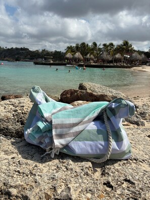 Eine Strandansicht mit einer Tasche auf Felsen, klarem Wasser und Palmen im Hintergrund.