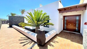 A modern house with a stone wall, a palm tree, and a wooden door. - Playas Blanca Pool Private Villas (Yaiza)