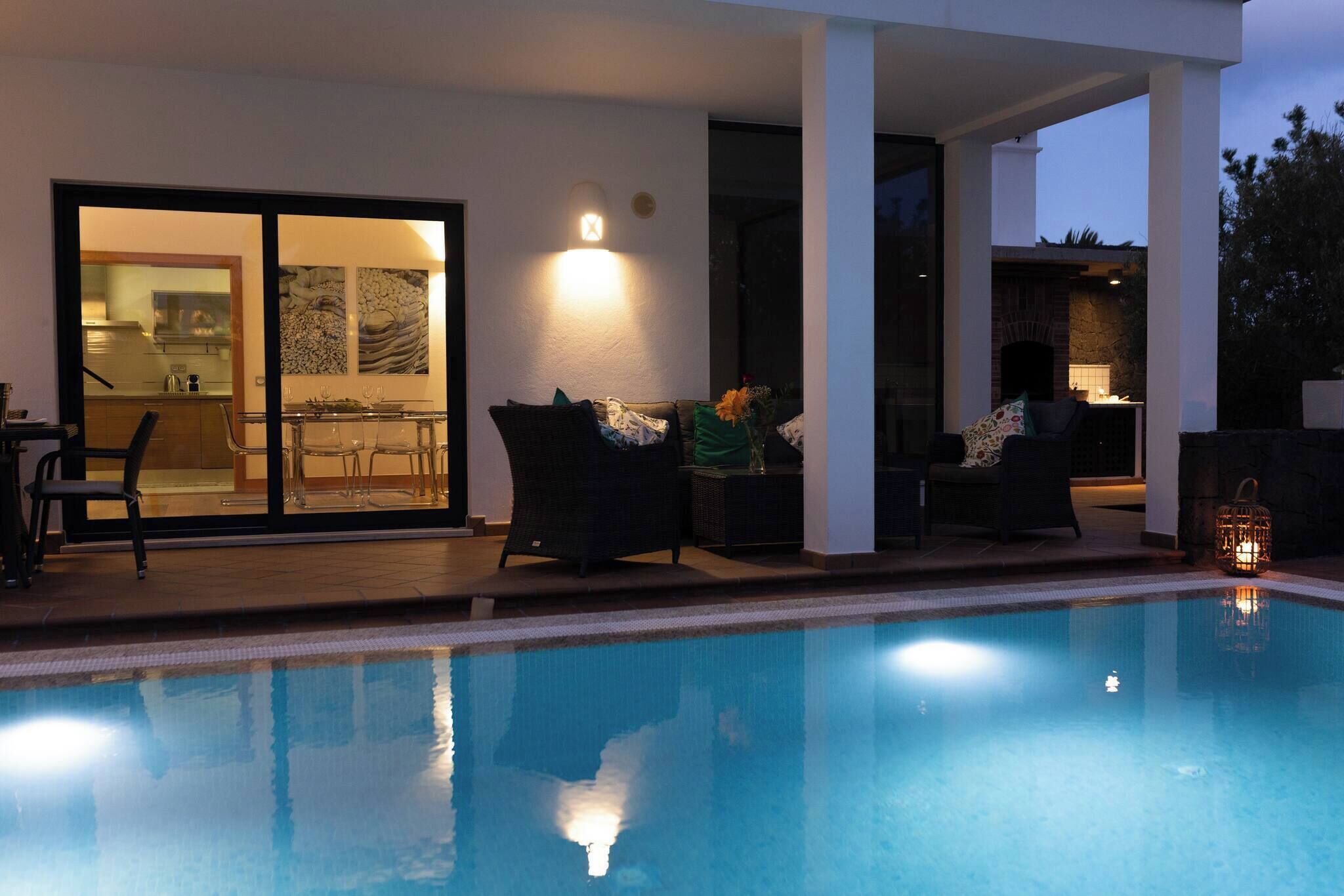 Une piscine dotée d’une structure en verre, d’un espace extérieur aménagé et d’une cheminée.