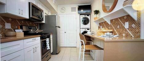 Cocina compacta con armarios blancos, microondas, estufa y lavadora.