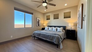 Un dormitorio con cama, ventilador de techo, ventana grande y obras de arte en las paredes.