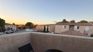 Terraza en la azotea con dos sillas plegables negras y una mesita redonda, con vistas a una zona residencial con casas y coches aparcados.