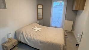 Un dormitorio con cama, mesita de noche, espejo, ventana con cortinas y ventilador de techo.