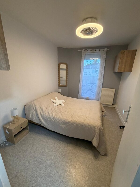 A bedroom with a bed, a nightstand, a mirror, a window with curtains, and a ceiling fan.