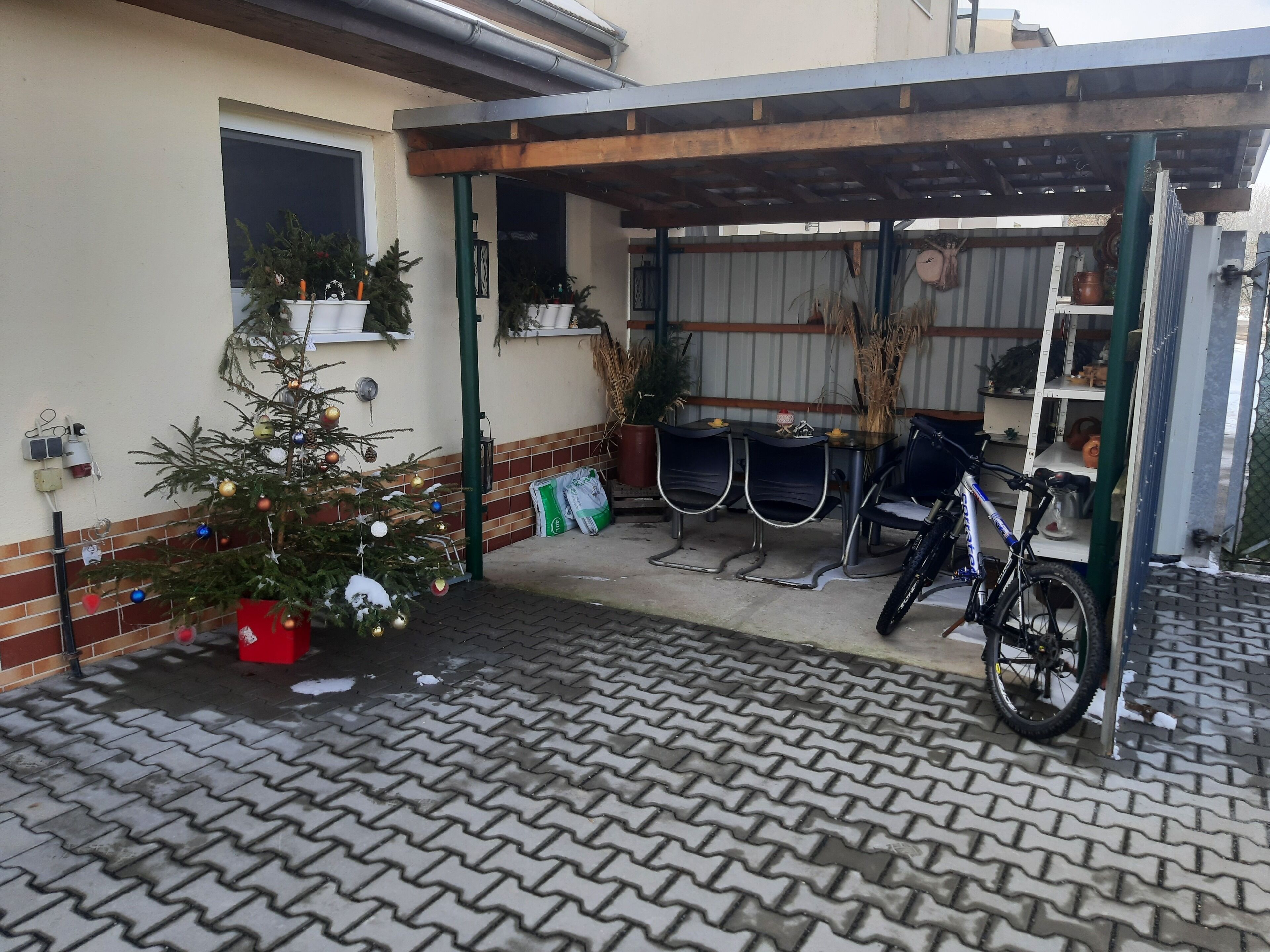 A covered outdoor area with a bicycle, a Christmas tree, and a small table with chairs.