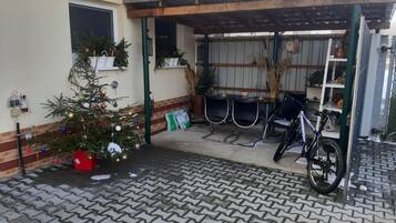 A covered outdoor area with a bicycle, a Christmas tree, and a small table with chairs.