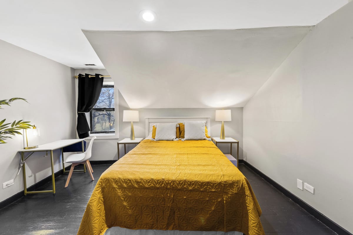 A hotel room with a large bed, a desk, a chair, and a window with curtains.