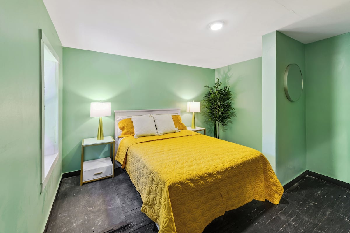 A hotel room with a bed, two bedside tables, a nightstand, a potted plant, and a mirror on the wall.