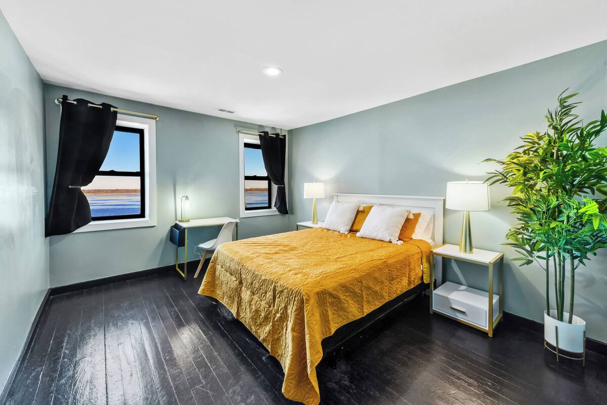 A hotel room with a bed, two bedside tables, a potted plant, and a view of the sea.