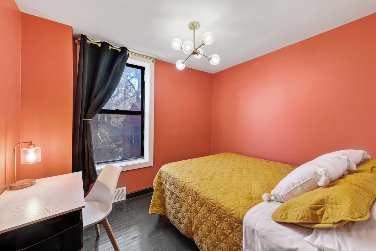 A room with a bed, a desk, a chair, a window with curtains, and a ceiling light.