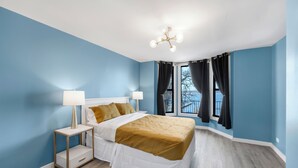 A bedroom with a bed, bedside tables, a lamp, a ceiling light fixture, and a window with curtains. - Randolph Hotel  (Fox Lake)