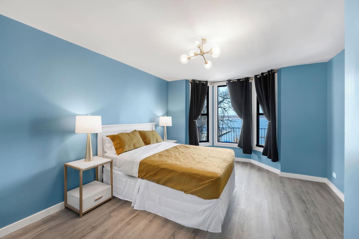 A bedroom with a bed, bedside tables, a lamp, a ceiling light fixture, and a window with curtains.