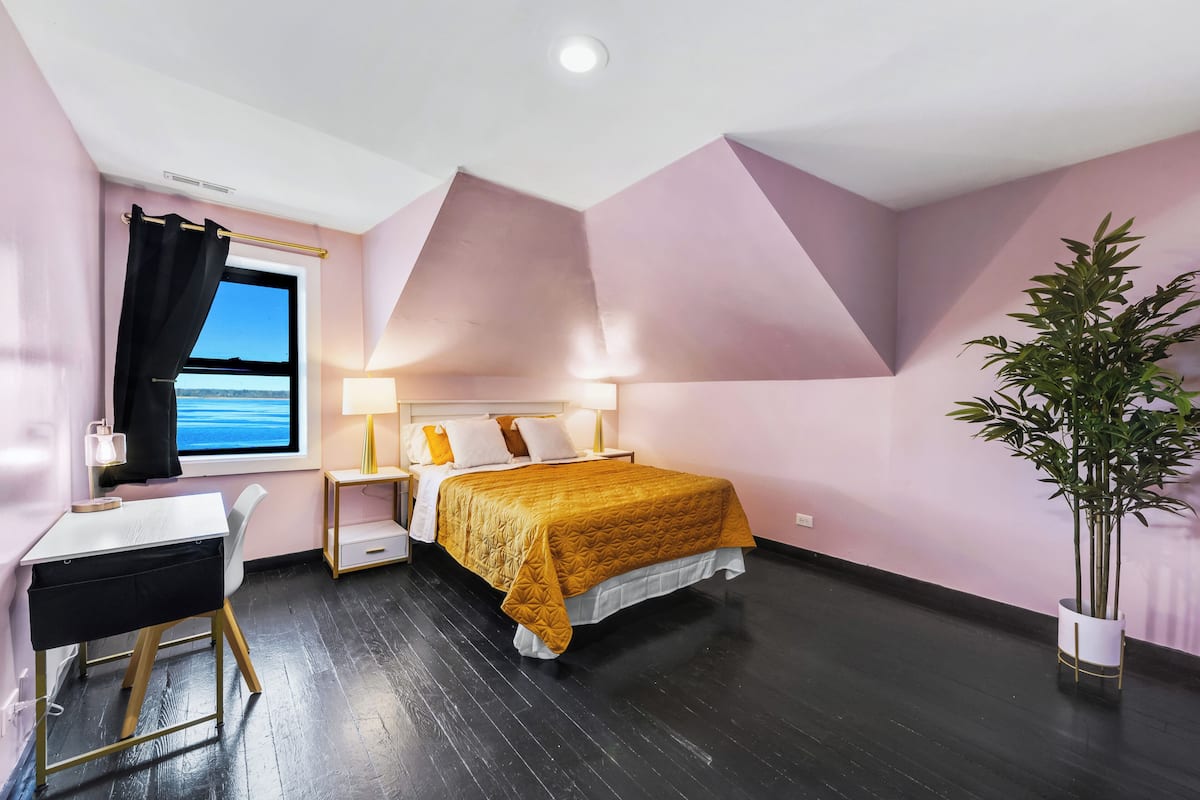 A bedroom with a bed, a desk, a chair, a window with a view, and a potted plant.