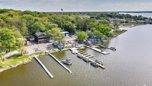 An aerial view of a lakeside property with docked boats, a parking area, and a small building. - Randolph Hotel  (Fox Lake)