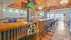 A bar area with a wooden counter, bar stools, and a chandelier. - Randolph Hotel  (Fox Lake)