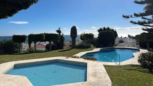 Two swimming pools with clear blue water, surrounded by well-maintained grass and trees, with a view of the sea in the background. - Luxury house in MOJÁCAR (Mojácar)
