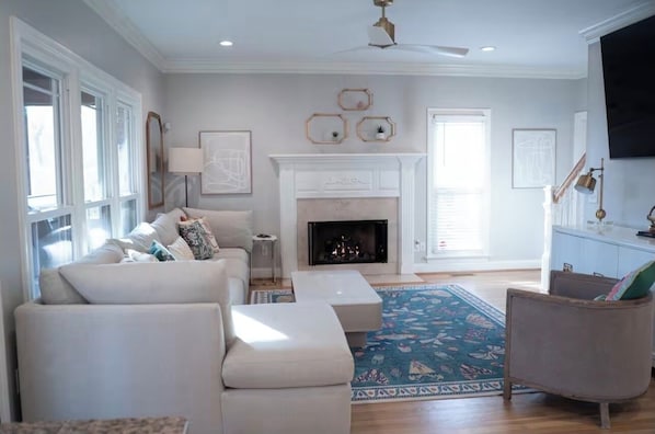 A spacious living room with a fireplace, a large window, and a blue patterned rug. - Stylish 5 bedroom/3b close to HPU, Wyndham & FM! (Jamestown)