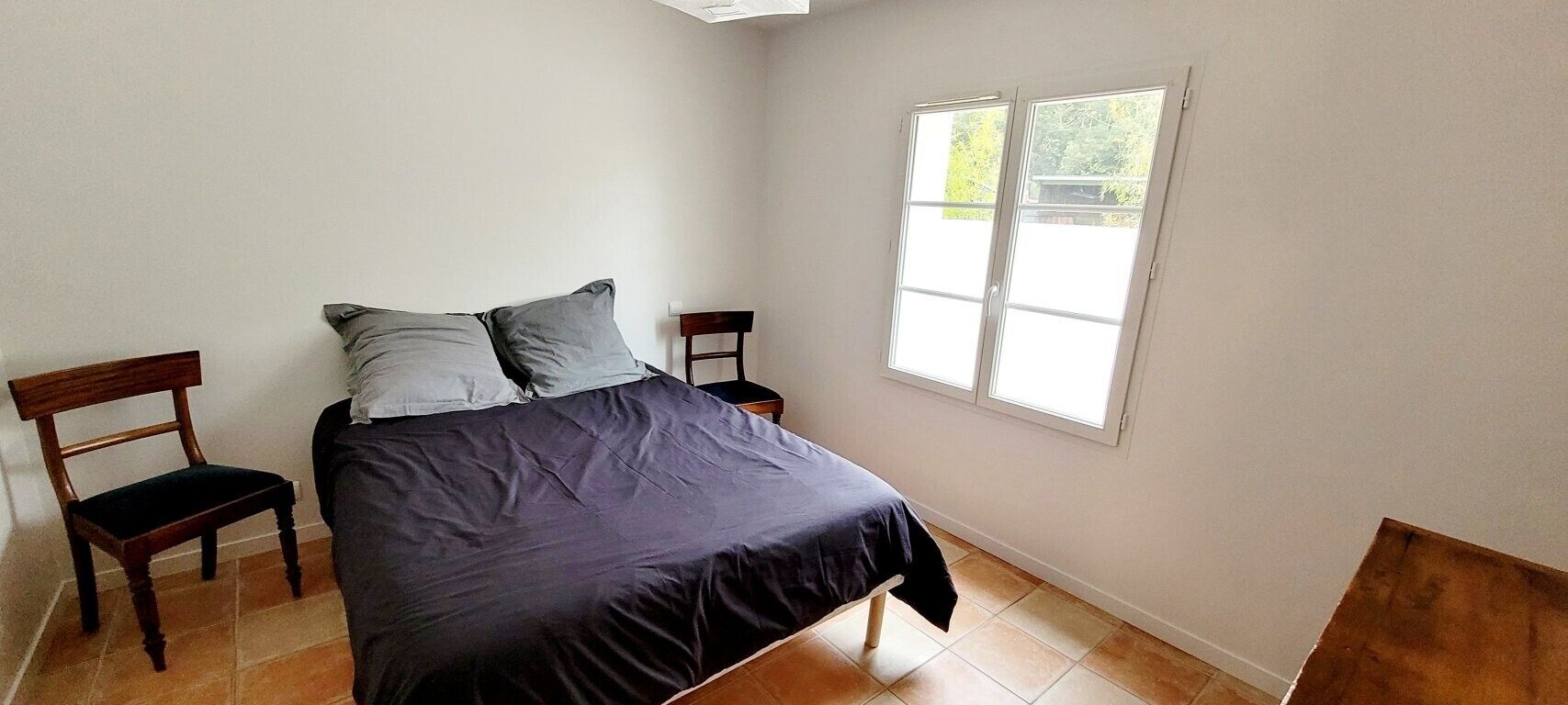 Een slaapkamer met een bed, twee nachtkastjes, een stoel en een raam.