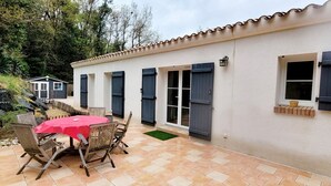 A patio with a table and chairs, a small shed, and a building with windows and shutters. - La maison des conches - ref 803 (Longeville-sur-Mer)