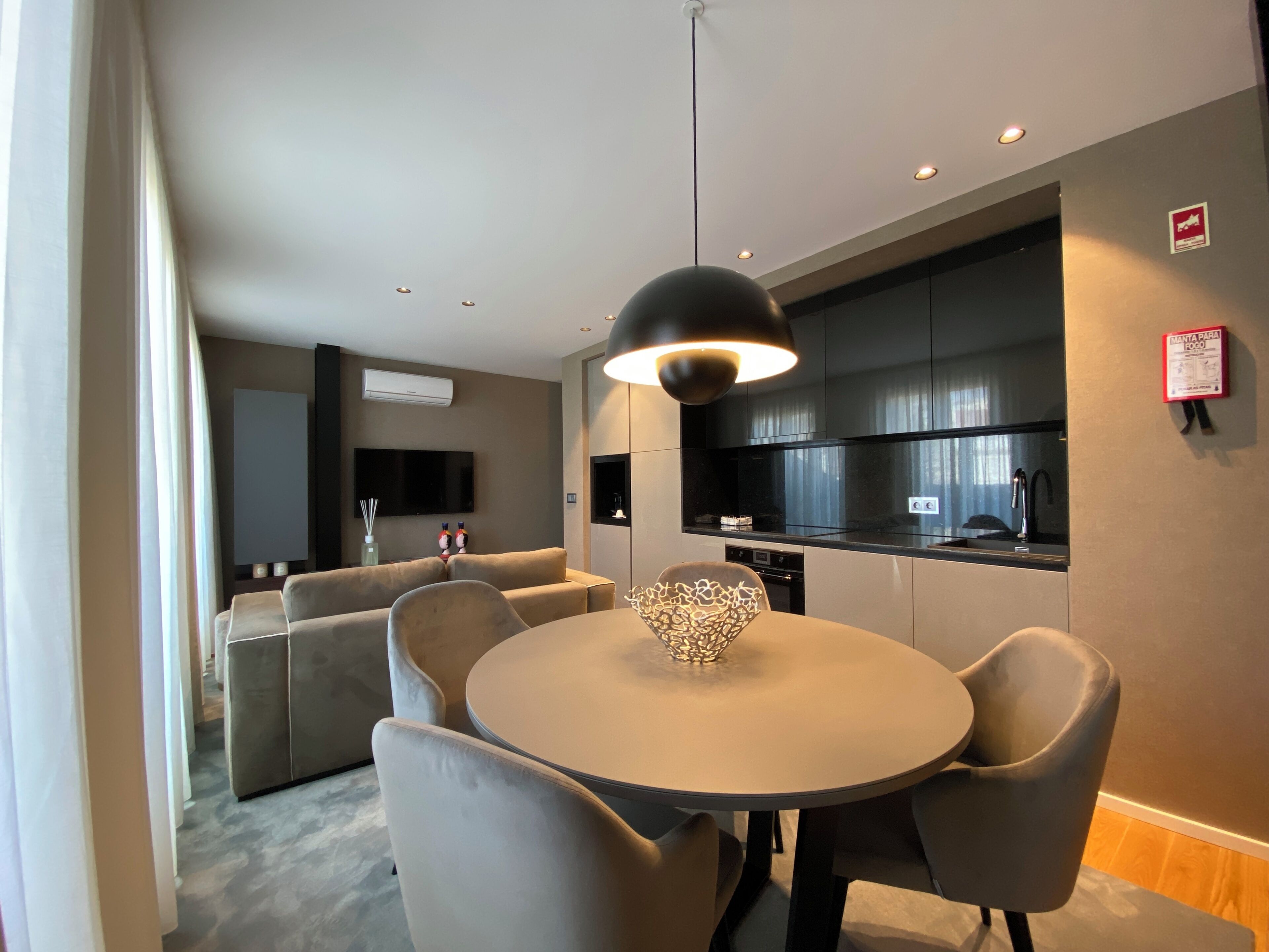A modern living room with a round dining table, grey sofas, and a black pendant light.