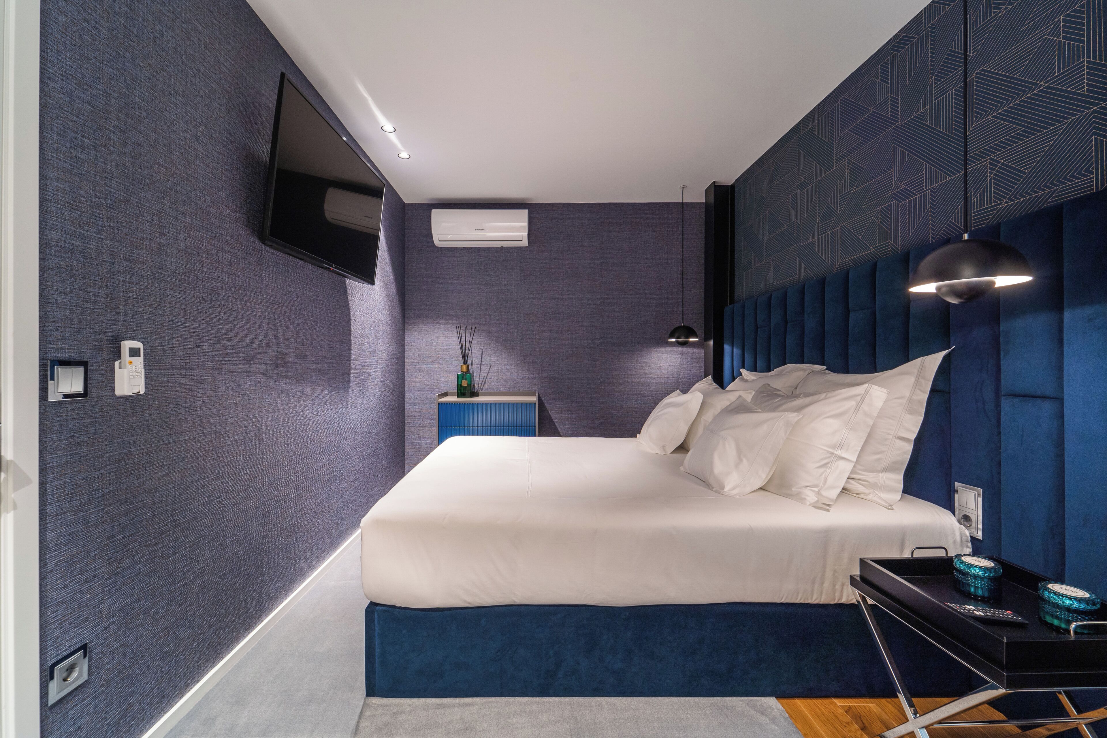 Une chambre moderne dotée d’un grand lit, d’un téléviseur à écran plat, d’un climatiseur et d’une table de chevet avec une lampe.