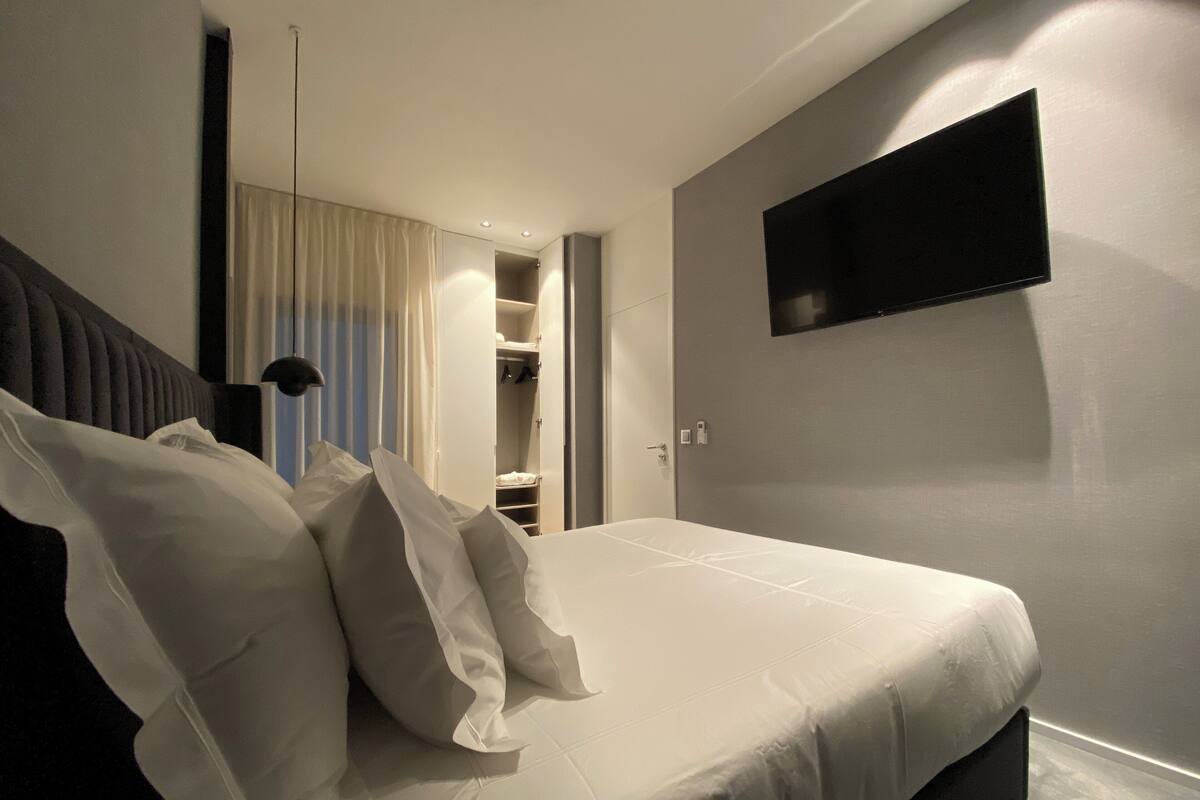 A modern bedroom with a bed, a TV mounted on the wall, and a walk-in closet.