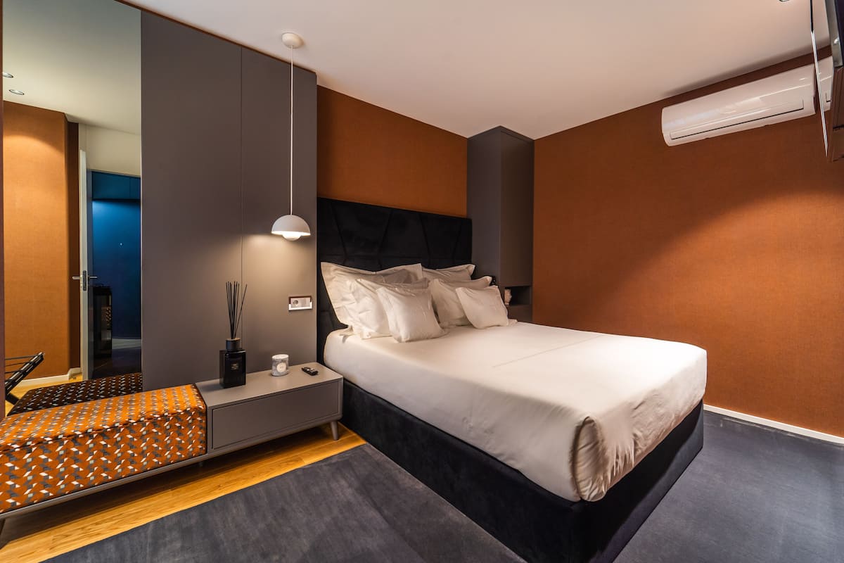 A modern bedroom with a bed, bedside table, lamp, and an air conditioning unit.
