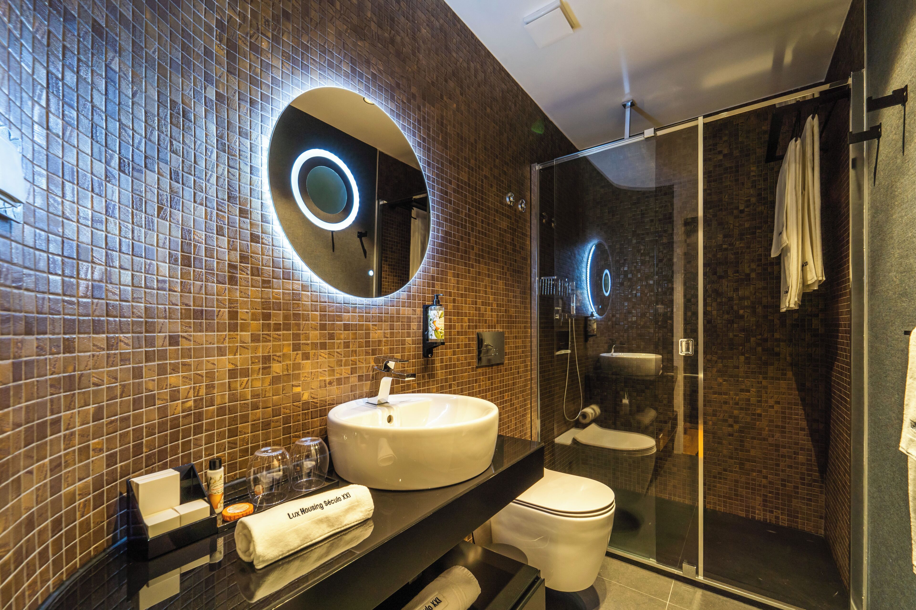 A modern bathroom with a round mirror, a sink, a toilet, and a glass shower enclosure.