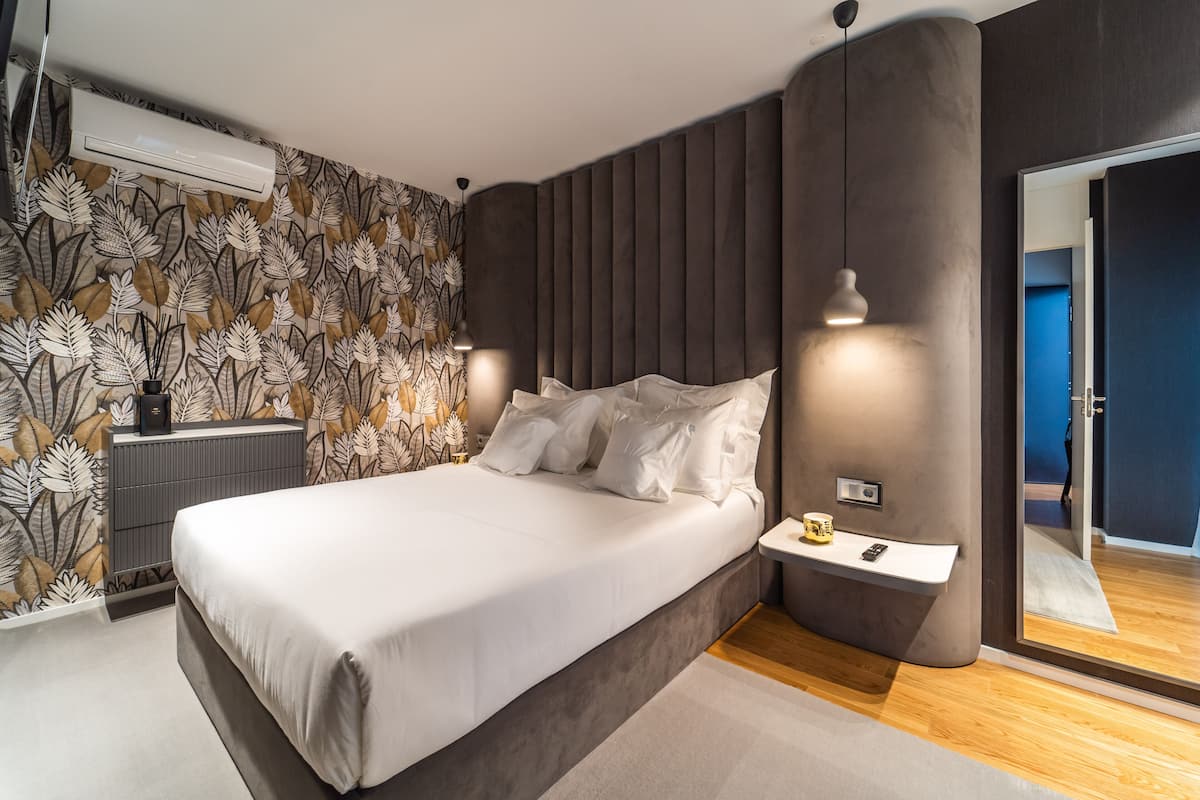 A modern bedroom with a large bed, a bedside table, a mirror, and a wall-mounted air conditioner.